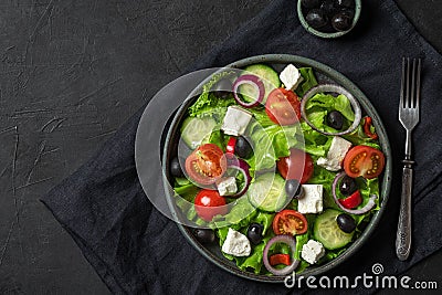 Fresh greek salad with olives, feta cheese, tomato, cucumber, onion with fork on towel on black background. top view Stock Photo