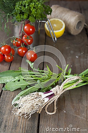 Fresh green garlic spears and arugula on wooden table with tomatoes and lemon Stock Photo