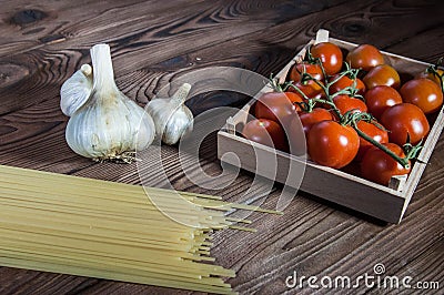 Fresh healthy cherry tomatoes, pasta spaghetti and garlic on wooden brown handmade cutting board Stock Photo