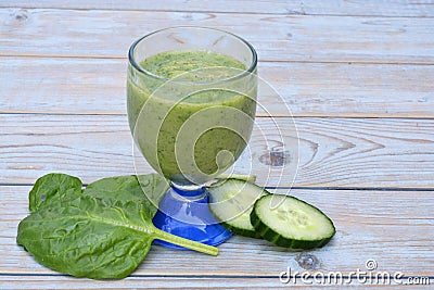 A fresh healthy green smoothie, cucumber slices, and a spinach leaf on a wooden table Stock Photo