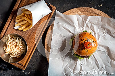 Fresh homemade burger on little cutting board with grilled potatoes, served with ketchup sauce and sea salt over wooden table with Stock Photo