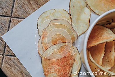 Fresh homemade deep fried crispy potato chips in white box on a wooden background, top view. Salty crisps scattered on a table for Stock Photo