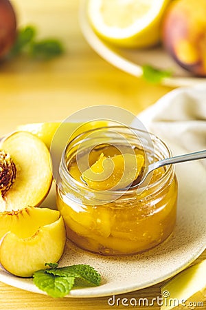 Fresh homemade peach jam in glass jar on a wooden background. Several fresh berries, lemon and mint are near it Stock Photo