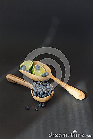 Fresh juicy blueberry fruits with limes on a wooden spoon against a dark background. Stock Photo