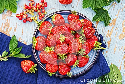 fresh juicy strawberries in a blue plate on an old wooden rural table, next to it is a dark blue napkin and mint leaves and Stock Photo