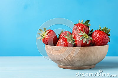Fresh juicy strawberries in wood bowl on light blue table Stock Photo