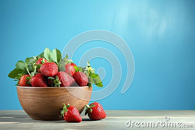 Fresh juicy strawberries in wood bowl on light blue table Stock Photo