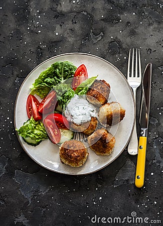 Fresh kale, tomato salad and canned tuna potato fish balls with greek yogurt cilantro sauce on dark background, top view Stock Photo