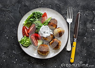 Fresh kale, tomato salad and canned tuna potato fish balls with greek yogurt cilantro sauce on dark background, top view Stock Photo