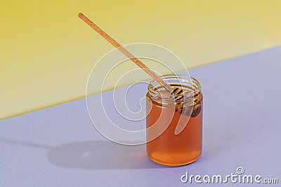 Fresh liquid honey jar with wooden dipper on grey and yellow Stock Photo