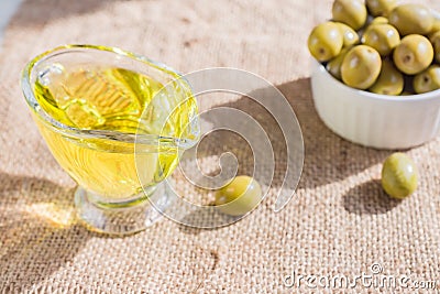 Fresh marinated green olives in white ceramic bowl and sauceboat of premium virgin olive oil on burlap cloth background Stock Photo