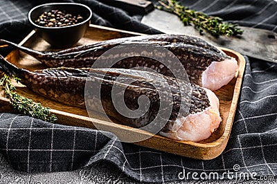 Fresh monkfish without a head on a wooden tray with a cleaver. Gray background. Top view Stock Photo