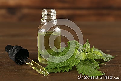 Fresh nettle leaves near glass bottle and pipette with oil on wooden table, closeup Stock Photo