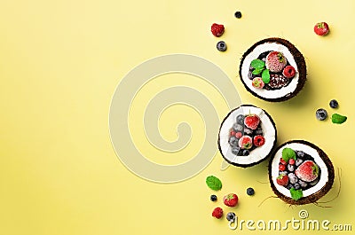 Fresh organic berries, mint leaves inside ripe coconuts on yellow background with copy space. Top View. Pop art design Stock Photo