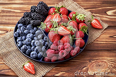 Fresh organic blueberries, blackberries, strawberries, raspberries on a separate dish on a textured wooden background Stock Photo