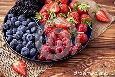 Fresh organic blueberries, blackberries, strawberries, raspberries on a separate dish on a textured wooden background Stock Photo