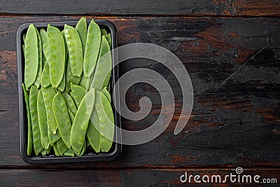 Fresh organic mangetout, also known as sugar snap pea, in plastic container, on old dark wooden table background, top view flat Stock Photo