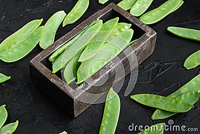 Fresh organic mangetout, also known as sugar snap pea, in wooden box, on black stone background Stock Photo