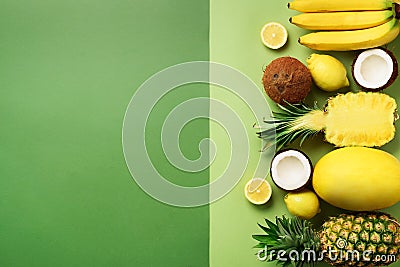 Fresh organic yellow fruits over green background. Monochrome concept with banana, coconut, pineapple, lemon, melon. Top Stock Photo