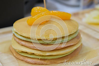 Fresh pancakes many color stacked layered with orange on wooden plate Stock Photo