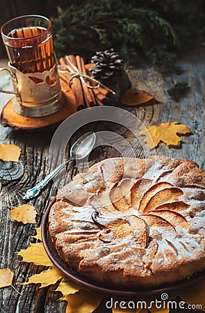 Fresh pastry apple pie with sugar powder on wooden table with hot drink tea and cinnamon on background. Homemade cake Thanksgiving Stock Photo