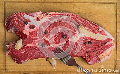 On a fresh piece of beef is a fork, garlic and pepper. Under it is an old cutting board Stock Photo