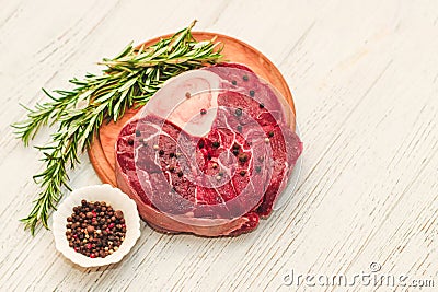 Fresh piece of meat large beef steak on the bone ossobuco with pepper, rosemary on the board. Stock Photo