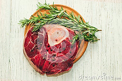 Fresh piece of meat large beef steak on the bone ossobuco with pepper, rosemary on the board. Stock Photo