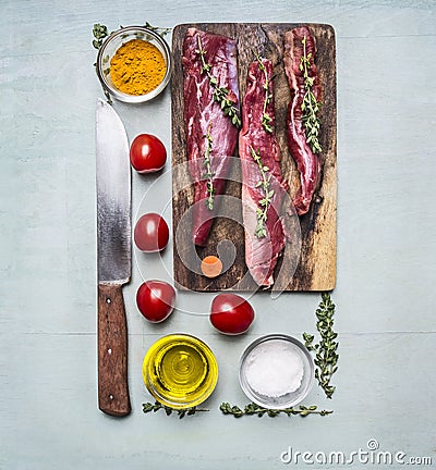 Fresh pieces of raw lamb on a chopping board, with herbs, spices, cherry tomatoes, lined rectangle on wooden rustic background top Stock Photo