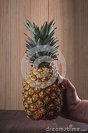Fresh Pineapple being held Vertical picture Ripe pineapple being held vertically by a strong male caucasian hand with a wooden ba Stock Photo