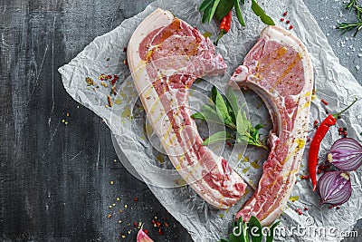 Fresh Pork middle cut ready to cook served with sage, red onion, chillies and red pepper drizzled with olive oil on Stock Photo