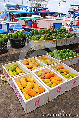 Fresh produce vendor selling papaya in boxes along Boduthakurufaanu Magu with large fishing vessel boats at Male, Maldives Editorial Stock Photo