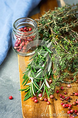 Fresh Provence Herbs Rosemary Thyme Twigs red Pink Peppers in Glass Jar on Aged Wood Cutting Board on Dark Concrete Stone Table Stock Photo