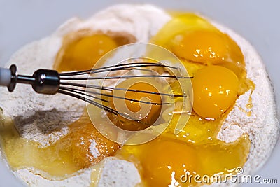 Fresh raw chicken eggs in flour close-up. Mix the broken raw eggs and wheat flour with a whisk to make the dough. The concept of h Stock Photo