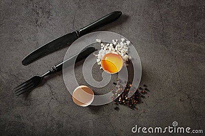 Fresh, raw chicken eggs with mushrooms and herbs, a fork and a knife on a black dish on a gray stone background, top view. Ingredi Stock Photo