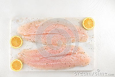 Fillet of sea bass and slices of pink lemon close up on a marble cutting board on white background Stock Photo