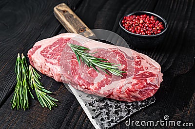 Fresh Raw new york strip beef steak on a butcher meat cleaver. Black wooden background. Top view Stock Photo