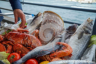 Fresh raw seafood presentation on cart at seaside restaurant with a man hand including fishes, prawn, shell, etc. on blurred ocean Stock Photo