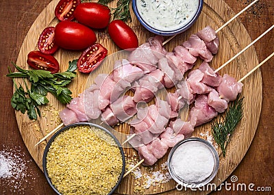 Fresh raw sliced turkey breast on skewer with bulgur, with tomato sauce and herbs with salt on a cutting board on a wooden backgr Stock Photo