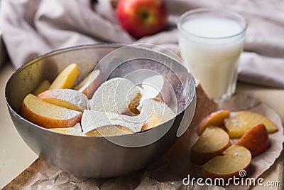 Fresh red apples sprinkled with flour in a stylish iron dish lying on a white window sill. Apple slices and a glass of Stock Photo