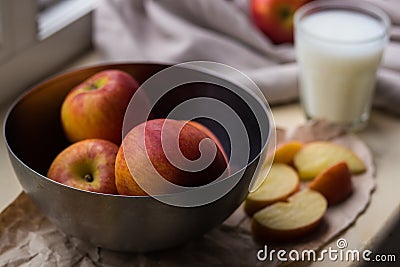 Fresh red apples in a stylish iron dish lying on a white window sill. Apple slices and a glass of milk are used as Stock Photo