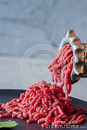 Fresh red meat mincing with old metal manual grinder, viewed in close-up on grey stone background . Stock Photo