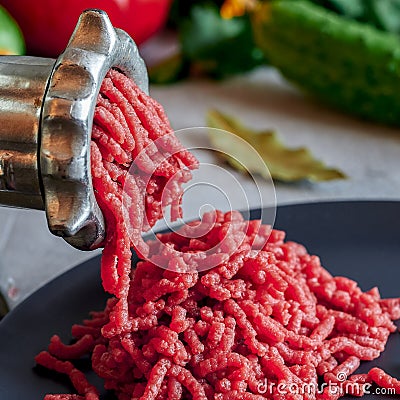 Fresh red meat mincing with old metal manual grinder, viewed in close-up on grey stone background . Stock Photo