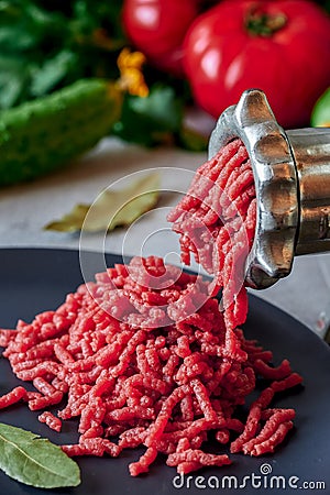 Fresh red meat mincing with old metal manual grinder, viewed in close-up on grey stone background . Stock Photo