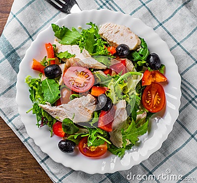 Fresh salad with chicken breast, arugula, black olives,red pepper, lettuce, fresh sald leaves and tomato on a white plate on woode Stock Photo