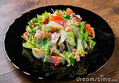 Fresh salad with fish, arugula, eggs,red pepper, lettuce, fresh sald leaves and tomato on a black plate on wooden table Stock Photo