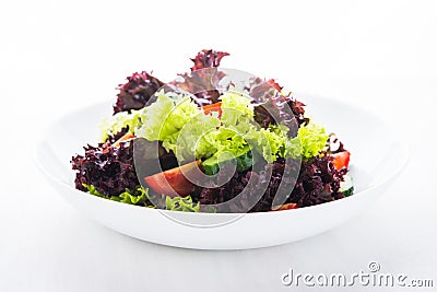 Fresh salad with green and purple lettuce, tomatoes and cucumbers on white wooden background close up. Stock Photo