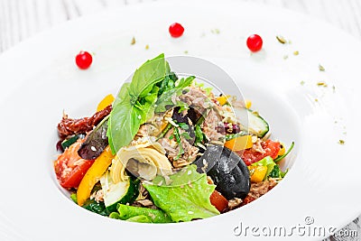 Fresh salad with tuna, arugula, artichokes, codfish, olives, basil, sun dried tomatoes, cherry tomatoes on wooden background Stock Photo