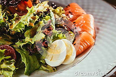 Fresh salad with vegetables, eggs and salmon served on white plate Stock Photo