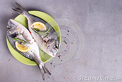 Fresh sea fish with spices and lemon ready for cooking on plate. Dorado or sea bream fish on stone background. Flat lay Stock Photo